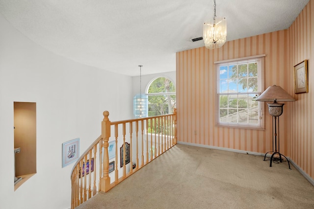 hall with carpet, a healthy amount of sunlight, an inviting chandelier, and a textured ceiling