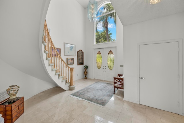 tiled foyer with french doors, a notable chandelier, and a towering ceiling