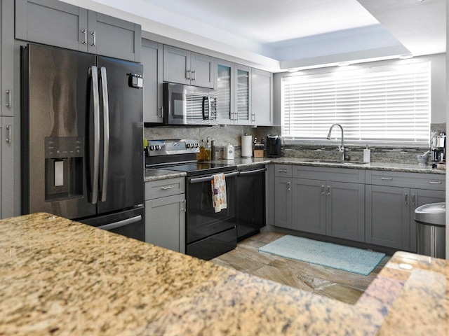 kitchen with sink, backsplash, appliances with stainless steel finishes, and light stone countertops