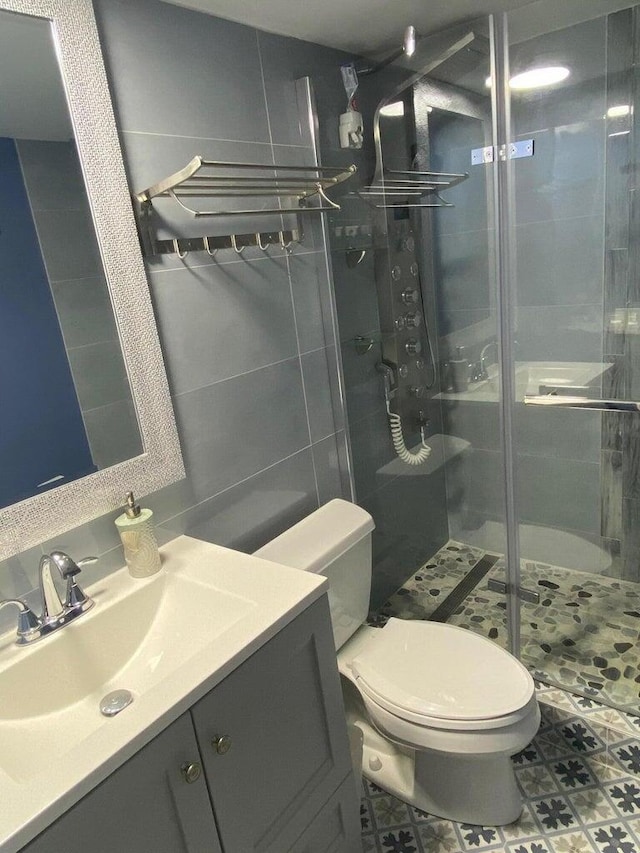 bathroom with a shower with shower door, tile patterned flooring, tile walls, vanity, and toilet