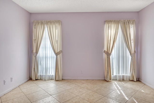 tiled empty room with a textured ceiling and a healthy amount of sunlight