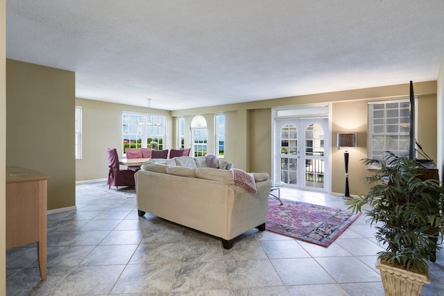 living area featuring a textured ceiling, baseboards, a notable chandelier, and tile patterned floors