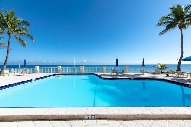 community pool featuring a patio area, fence, and a water view