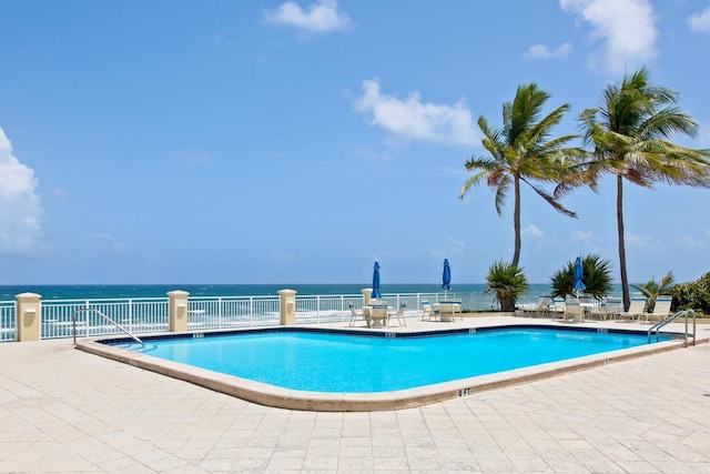 community pool featuring a patio, a water view, and fence