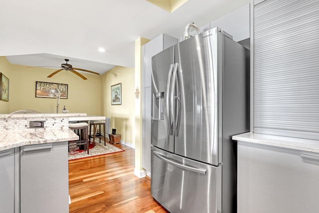 kitchen featuring light stone countertops, baseboards, light wood finished floors, ceiling fan, and stainless steel fridge