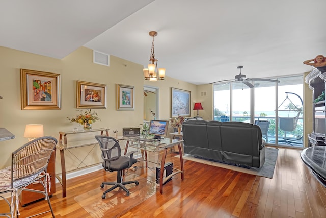 office featuring ceiling fan with notable chandelier, visible vents, wood-type flooring, and expansive windows