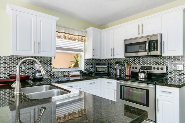 kitchen featuring backsplash, dark stone counters, stainless steel appliances, and white cabinetry