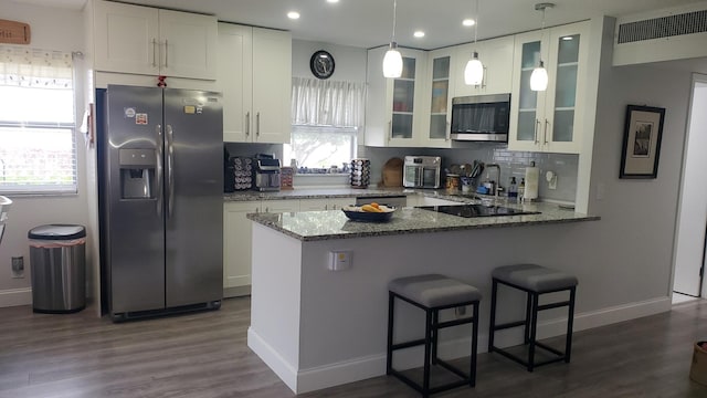 kitchen featuring dark hardwood / wood-style floors, stainless steel appliances, white cabinetry, dark stone countertops, and tasteful backsplash