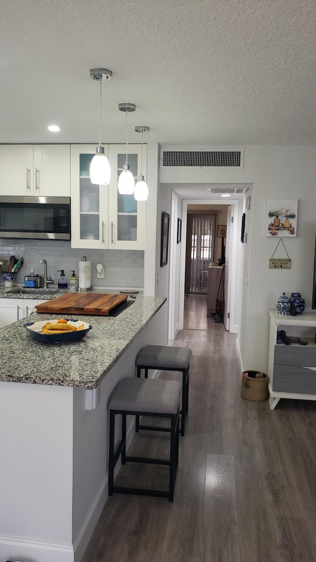 kitchen with a kitchen breakfast bar, light stone counters, dark hardwood / wood-style flooring, and white cabinetry