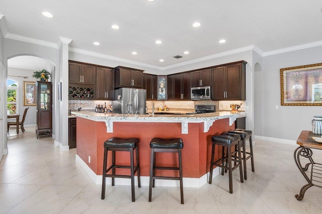 kitchen featuring a kitchen island with sink, ornamental molding, stainless steel appliances, and light stone countertops