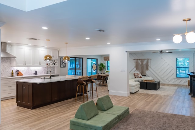 kitchen with pendant lighting, white cabinetry, a kitchen island with sink, and wall chimney range hood