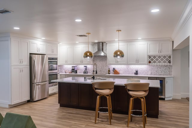 kitchen featuring hanging light fixtures, wall chimney range hood, stainless steel appliances, and white cabinets