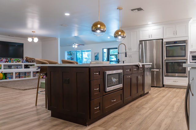 kitchen featuring stainless steel appliances, a breakfast bar, hanging light fixtures, and a center island with sink