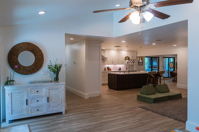 kitchen with decorative light fixtures, an island with sink, wood-type flooring, white cabinets, and decorative backsplash