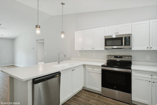 kitchen featuring hanging light fixtures, vaulted ceiling, appliances with stainless steel finishes, sink, and kitchen peninsula