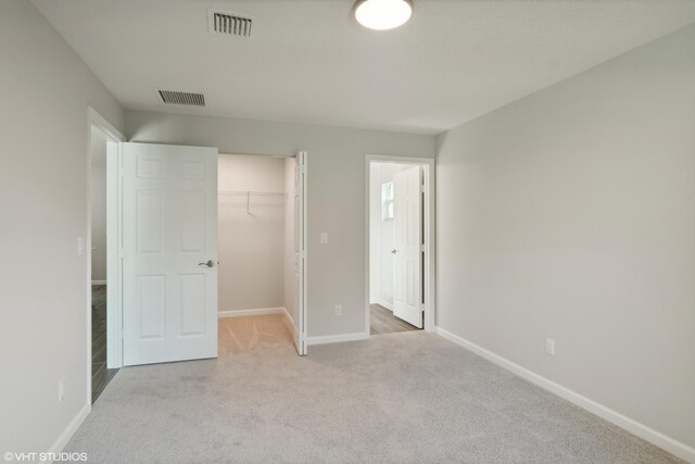 unfurnished bedroom featuring a walk in closet, light carpet, and a closet