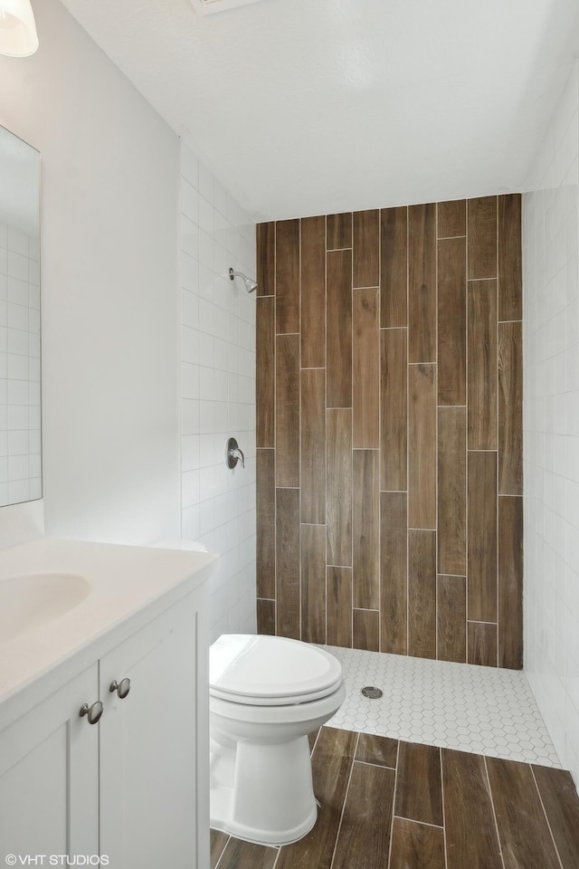 bathroom with tile walls, vanity, tiled shower, and toilet