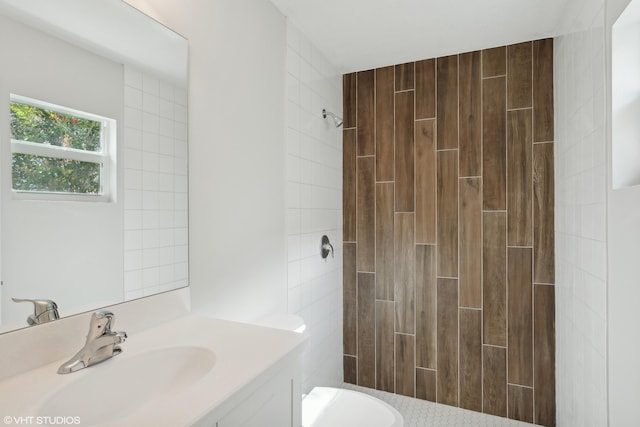 bathroom with toilet, a tile shower, and vanity