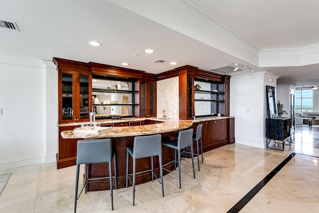 kitchen with light tile patterned flooring, crown molding, kitchen peninsula, and light stone counters