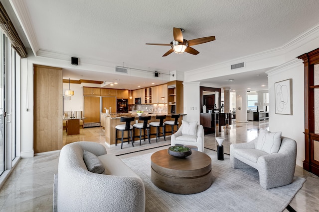 tiled living room with ceiling fan, decorative columns, crown molding, and a textured ceiling