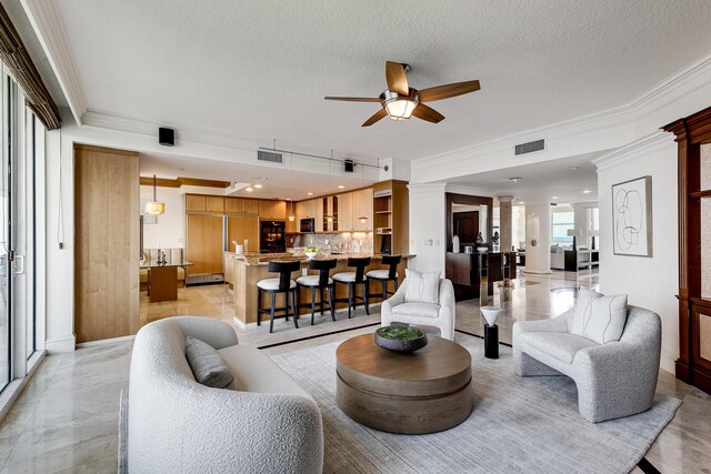 living area with a textured ceiling, a ceiling fan, visible vents, and crown molding