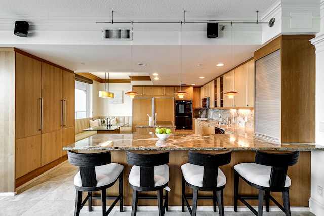 kitchen with hanging light fixtures, light stone counters, decorative backsplash, kitchen peninsula, and black appliances