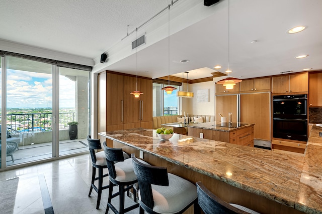 kitchen featuring black double oven, pendant lighting, light tile patterned floors, stone counters, and crown molding