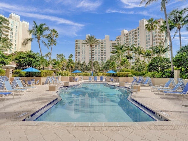 community pool with a patio area, a view of city, and fence