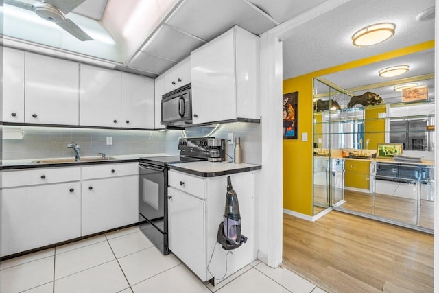 kitchen featuring white cabinets, black appliances, light wood-type flooring, tasteful backsplash, and sink