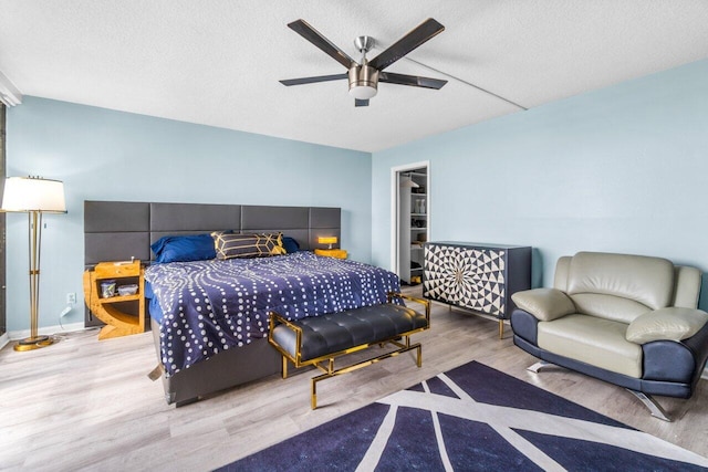 bedroom featuring ceiling fan, a spacious closet, a textured ceiling, and light hardwood / wood-style floors