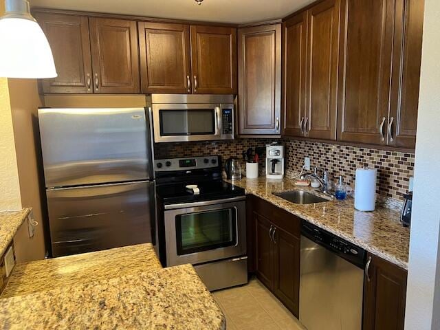 kitchen with tasteful backsplash, stainless steel appliances, light stone countertops, light tile patterned floors, and sink