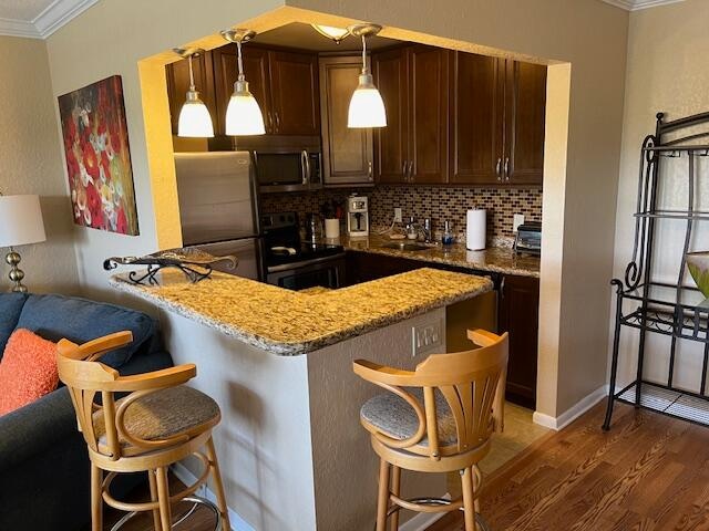 kitchen featuring stone counters, dark hardwood / wood-style floors, stainless steel appliances, decorative light fixtures, and tasteful backsplash