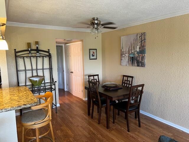 dining area with ceiling fan, dark hardwood / wood-style flooring, ornamental molding, and a textured ceiling