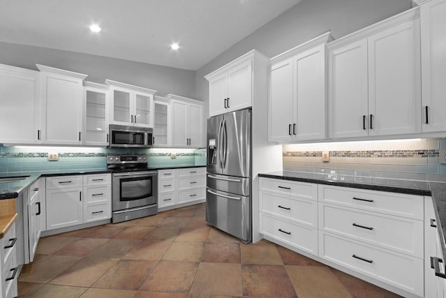 kitchen featuring appliances with stainless steel finishes, dark tile patterned floors, white cabinets, and backsplash