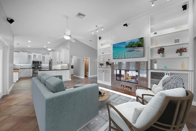 tiled living room featuring ceiling fan, vaulted ceiling, rail lighting, and built in shelves