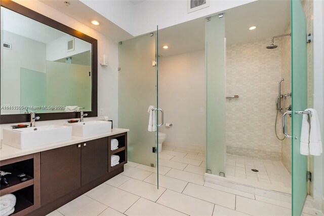 bathroom with double sink vanity, a shower with door, toilet, and tile patterned floors