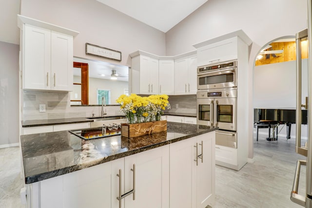 kitchen featuring decorative backsplash, sink, double oven, a center island, and ceiling fan