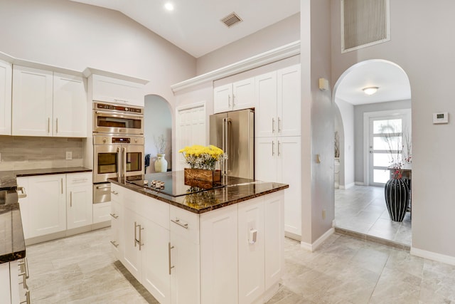 kitchen with appliances with stainless steel finishes, decorative backsplash, light tile patterned floors, a center island, and vaulted ceiling