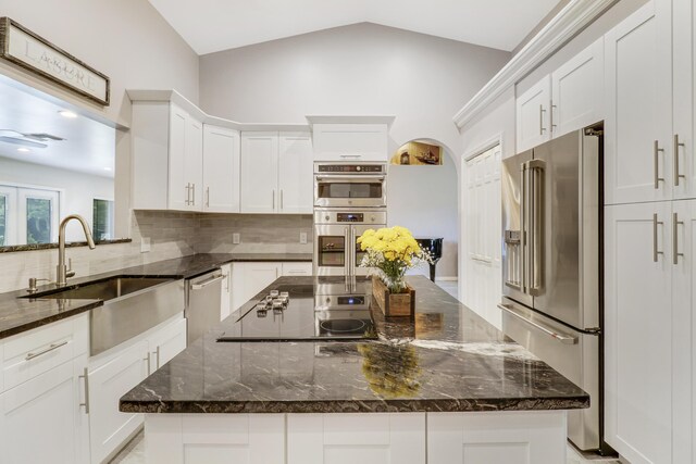 kitchen featuring appliances with stainless steel finishes, dark stone countertops, a kitchen island, and lofted ceiling