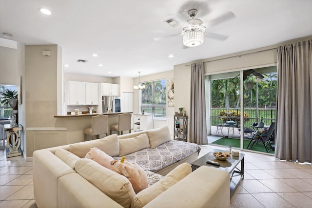 tiled living room with ceiling fan with notable chandelier