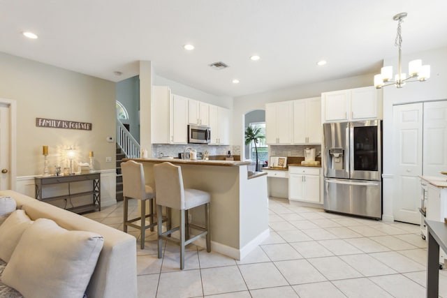 kitchen with appliances with stainless steel finishes, backsplash, white cabinets, light tile patterned floors, and a breakfast bar area