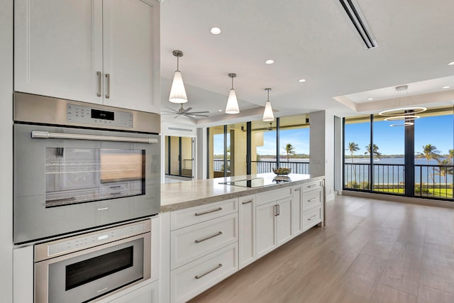 kitchen featuring double wall oven, cooktop, white cabinetry, light hardwood / wood-style floors, and light stone countertops