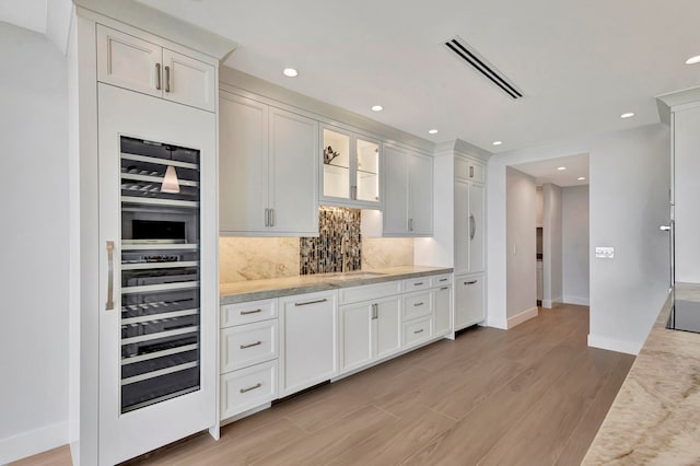 kitchen with sink, tasteful backsplash, light wood-type flooring, and light stone countertops