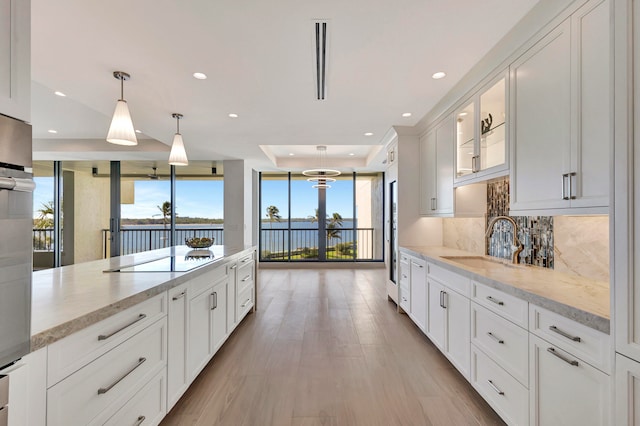 kitchen featuring black electric stovetop, backsplash, white cabinets, light stone counters, and sink