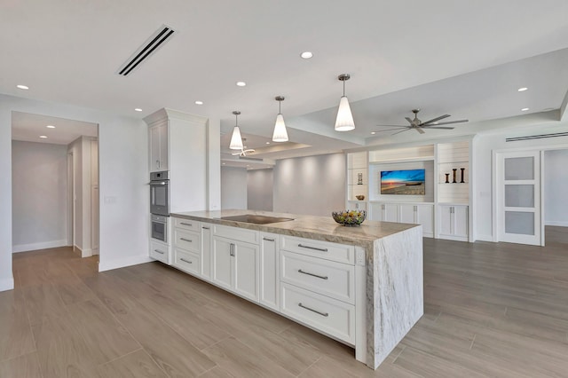 kitchen featuring hanging light fixtures, white cabinetry, light stone countertops, light hardwood / wood-style floors, and double oven