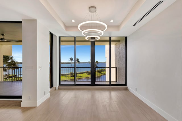 empty room featuring light wood-type flooring, ceiling fan with notable chandelier, a tray ceiling, and a water view