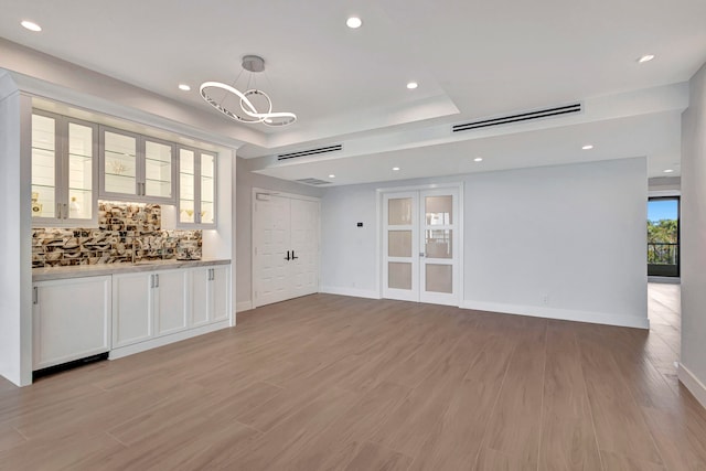 unfurnished living room with a notable chandelier, a raised ceiling, and light hardwood / wood-style flooring