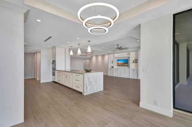 kitchen featuring stainless steel double oven, light stone countertops, ceiling fan with notable chandelier, white cabinetry, and pendant lighting