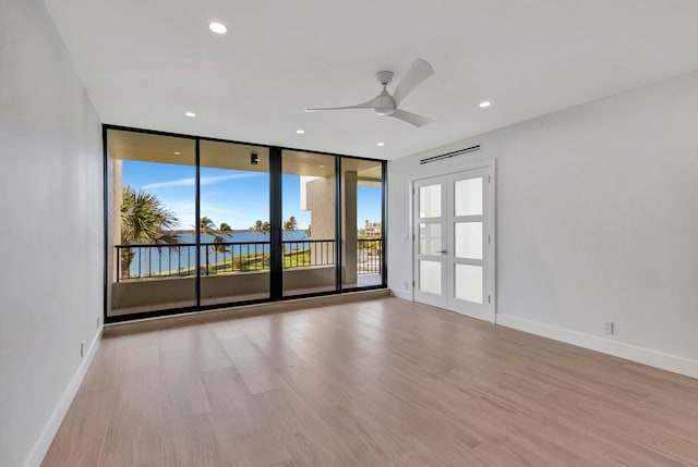 empty room featuring ceiling fan, light wood-type flooring, floor to ceiling windows, french doors, and a water view