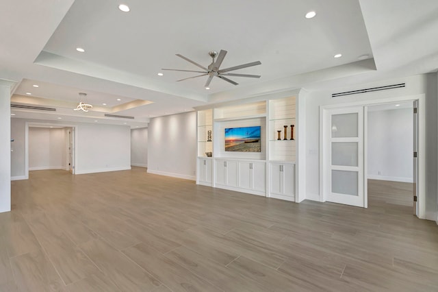 unfurnished living room featuring ceiling fan, light hardwood / wood-style floors, and a tray ceiling